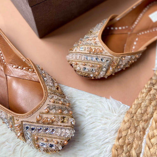 Handcrafted beige juttis embroidered with different types of stones, crystals, tassels and beads for Women.
