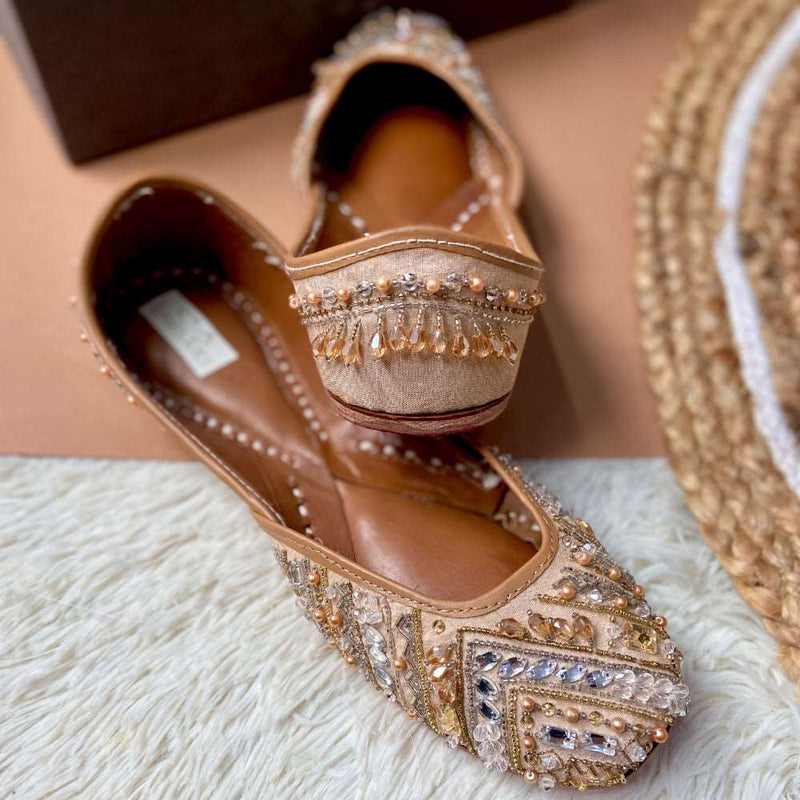 Handcrafted beige juttis embroidered with different types of stones, crystals, tassels and beads for Women.