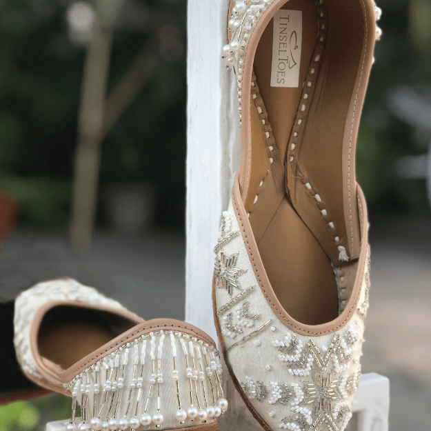 Ethnic handcrafted hand-embroidered Ivory juttis delicately embroidered with katdana, beadwork, silver pipes, zari, sequins, pearls and a beautiful tasselled back for women.