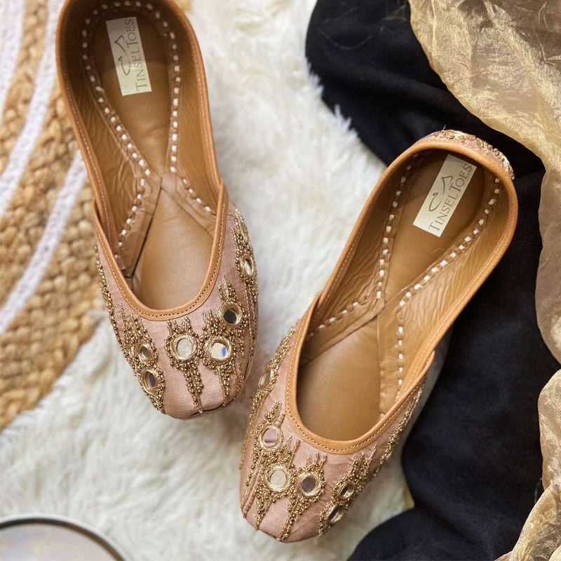 Handcrafted stylish nude juttis embellished with intricate mirror work and gold thread for women.